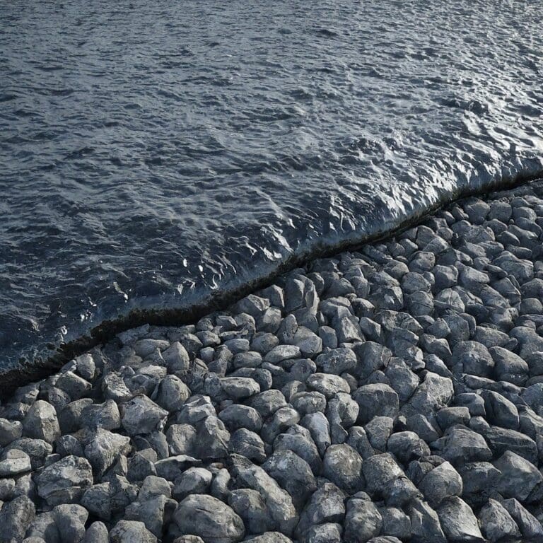A stone breakwater meets the calm waters of a body of water, with small waves gently lapping against the rocks.