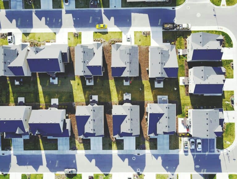 Aerial view of a suburban neighborhood showcasing rows of identical houses with driveways, cars, lawns, and clean streets.