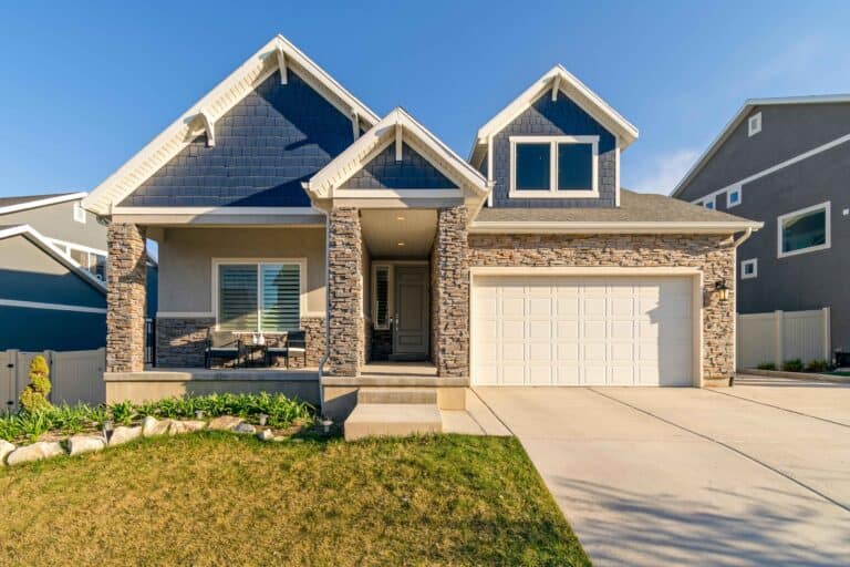 A modern suburban house with a stone facade, blue siding, white garage door, and a manicured lawn.